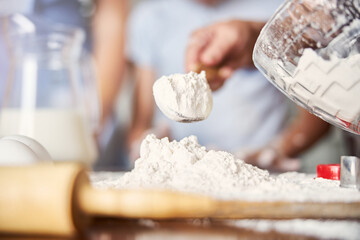 Baker tipping wooden spoon full of flour on table surface