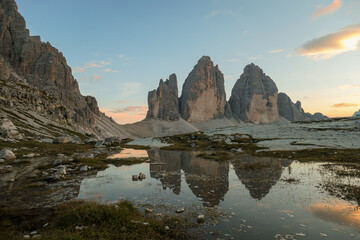 Golden hour over the Tre Cime di Lavaredo (Drei Zinnen), mountains in Italian Dolomites. The peaks reflect in a paddle. The mountains are surrounded with orange and pink clouds. Sunset time. Serenity