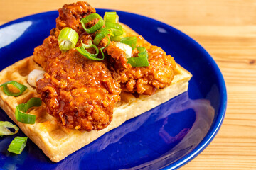 Homemade Southern American comfort street food fresh deep fried crispy stacked chicken wings with buffalo red chili spicy hot sauce and waffle sweet maple syrup