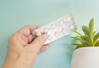 A woman's hand holds a blister with pills on a blue background, near a flower, Allergy prevention