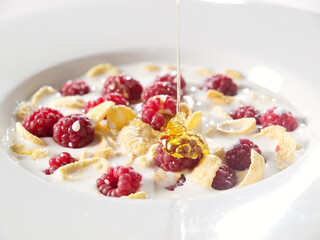honey corn flakes with fresh raspberry and pouring milk in bowl