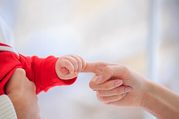 Close up Infant in santa claus suit gently holding mom finger. Baby squeezes parent hand on white background. Family and Mothers day concept. Christmas concept. Baby care. Happy childhood. copy space