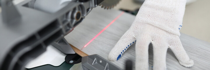 Close-up of qualified male worker cutting new wooden laminate. Big equipment for professionals. Prepare material for work. Protective gloves. Renovation and construction site concept