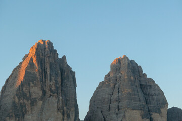 A close up view on the first sunbeams reaching the top of the Tre Cime di Lavaredo (Drei Zinnen), Italian Dolomites. The peaks shine with pink and orange. New day beginning.