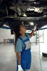 Young african american girl mechanic looking at bottom of car
