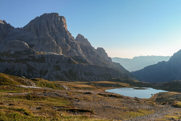 Fototapeta na wymiar A panoramic view on a vast valley in Italian Dolomites during early morning hours. The valley is surrounded with high mountains from each side. Small lake in the middle. Remote and isolated place.
