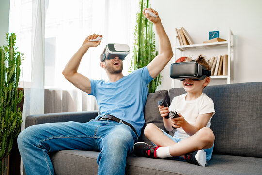 Dad and son sitting on sofa and playing games with VR glasses