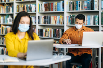 Education during quarantine. Students sit at a distance from each other with protective masks on their faces and study using a laptop
