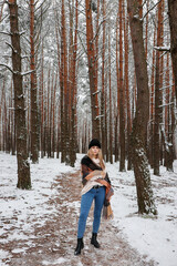 The woman is wearing a big warm scarf and a winter knitted hat. Outerwear on a woman. Snowy forest around.