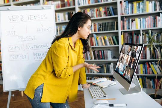 Young Smart Caucasian Woman Teacher Conducts An Online Lesson With Her Students Via Video Conference Telling Information On A Video Call