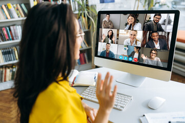 Computer monitor view over female shoulder during group video call with multi-ethnic international...