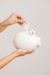Hand with Indian currency with piggy bank on white.
