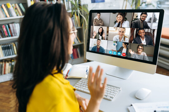 Computer monitor view over female shoulder during group video call with multi-ethnic international business colleagues discussing about future financial plans and strategy