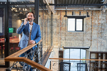 Smiley man talking on phone while standing in loft hotel