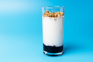 Bio yogurt with muesli and balck currant jam on blue background with copy space.