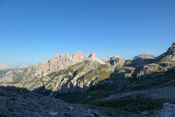 Obraz premium A view on a vast valley in Italian Dolomites. The valley is surrounded with high and sharp mountains from each side. Morning sun warms the valley up. Remote and isolated place. Remedy
