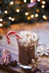 Cup of hot chocolate with marshmallow and candy cane in front of Christmas tree