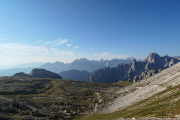Fototapeta premium A view on a vast valley in Italian Dolomites. The valley is surrounded with high and sharp mountains from each side. Morning sun warms the valley up. Remote and isolated place. Remedy