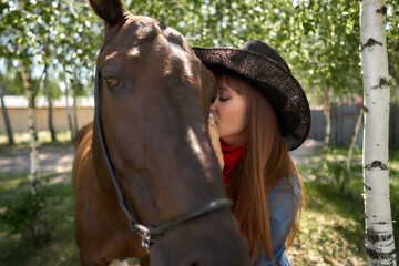 Fototapeta premium beautiful equestrian in hat hugging black horse at ranch