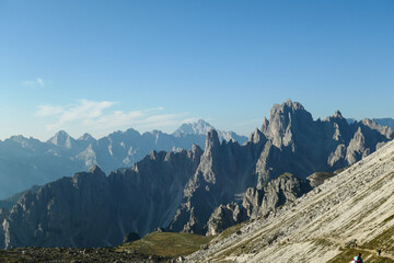 Fototapeta na wymiar Panoramic view on Italian Dolomites. Endless, high and sharp mountains from each side. The peaks are shrouded in morning haze. Narrow pathway going along the mountain slope. Remote and isolated place
