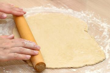 Women's hands roll out the dough with a rolling pin