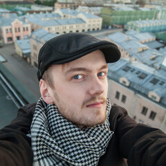 Portrait of smiling guy with beard and blue eyes in black cap on a sunset rooftop background