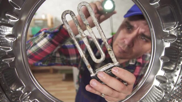 Close up of a repairman holding a broken heating element next to the washing machine