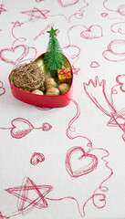 Holiday composition in a red heart-shaped box with a miniature Christmas tree, golden walnuts. Vertical photo.