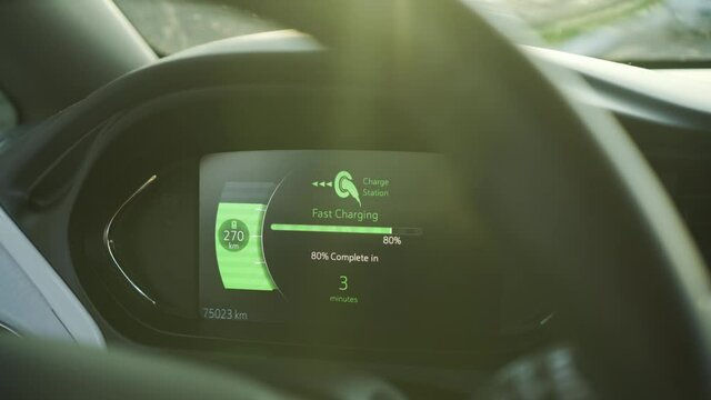 Electric car vehicle dashboard view during fast DC charging parked at power station. Green energy car interior view. Long range electric vehicle. Sunset light