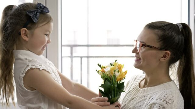 6-7 year old girl gives a bouquet of freesias and hugs her mother. Mom's Birthday or Mother's Day.