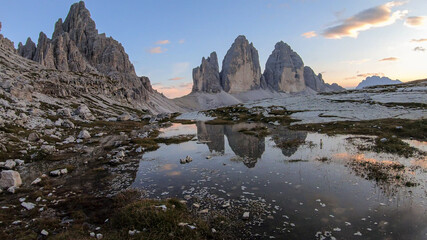 Fototapeta na wymiar A panoramic view on the Tre Cime di Lavaredo (Drei Zinnen), mountains in Italian Dolomites. The mountains are reflecting in small paddle. Desolated and raw landscape. Early morning. Daybreak