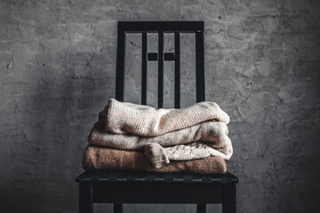 a stack of knitted warm cozy sweaters , on a chair by the gray wall. autumn, winter 