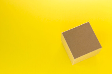 Small square cardboard box on yellow background. Delivery package. Top view, flat lay with copy space.