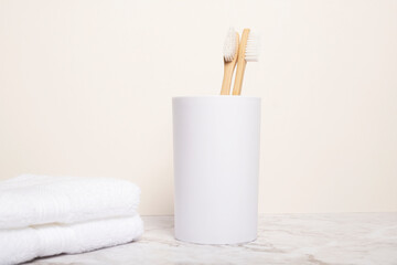 Two natural bamboo toothbrushes in a cup on a marble countertop with magnolia wall behind with copy space and room for text