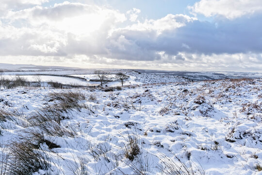 Low winter sun sends sunbeams through dark clouds over a snow covered  Derbyshirelandscape