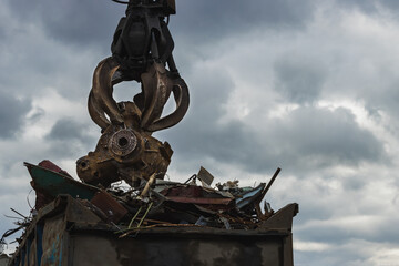 An excavator loads scrap metal into the back of a truck at a landfill or recycling center.