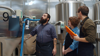Bearded man engineer showing two apprentice beer tanks in large brewery
