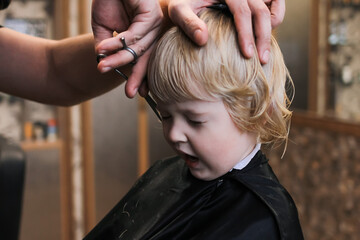 Fototapeta premium A little boy is trimmed in the barbershop. Bright emotions on the face, facial expression, the process of cutting hair.