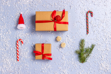 Gift boxes wrapped with paper kraft, red ribbon, branch of Christmas tree,  santa hat, balls,  candy on sticks on a light background. Top view. Presents for the holiday, Christmas
