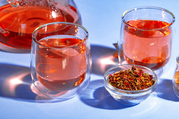 Glass teapot and glass cups of fruit tea on blue background