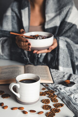 The woman is wrapped in a blanket and holds a smoothies on a plate in her hands. cup of coffee 