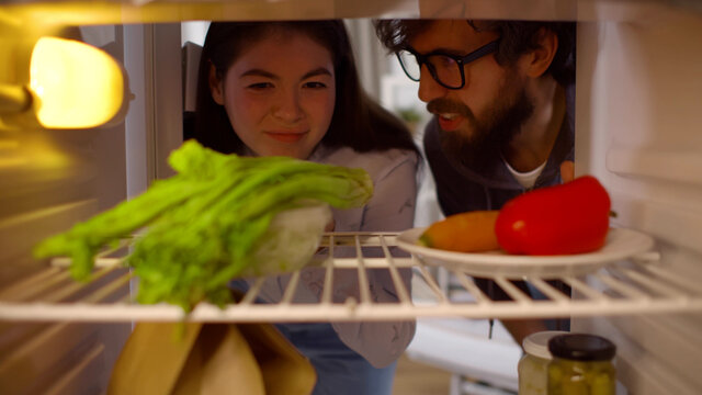 Hungry diverse couple on diet opening fridge and looking at vegetables - Powered by Adobe