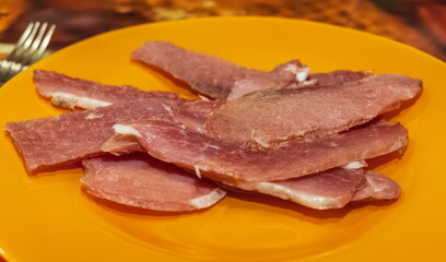 Thin slices of dried beef on an orange plate close-up against a colored oilcloth. The focus in the center