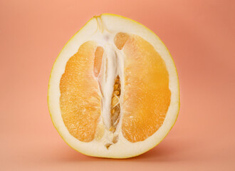 Half a juicy yellow pomelo on a peach background.