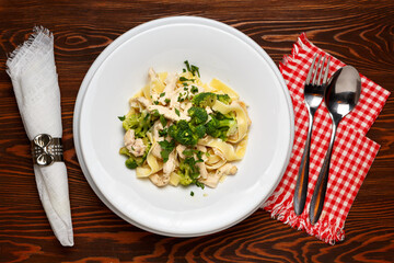 Pasta with broccoli and chicken on a white plate on a dark wooden table