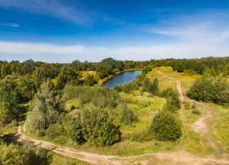Top view of the forest, road and pond against the blue sky and white clouds