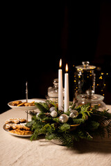Christmas decoration: two white candles and traditional cookies arranged on linen tablecloth. Black background with copy space for text. Holidays preparation and New Year celebration concept