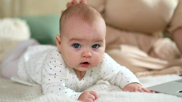 Cute sweet baby girl resting on bed with mom looking at camera with thoughtful eyes smiling enjoying connect. Family lifestyle. Health care concept. Female child innocence. Sunny background.