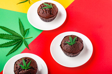 Marijuana chocolate cupcake muffins with weed cbd. Medical marijuana hemp drugs in food dessert. Weed muffins with cannabis and cannabis leaves served on rastaman flag red background Copy space.