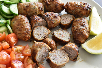 Sheftalia: Cypriot Lamb and Pork Sausages.  Grilled Sausages with Fresh Vegetables (Cucumber and Tomato) on a White Plate. Traditional Cypriot food. 